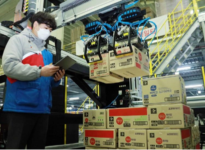 A CJ Logistics employee stands next to a stack of inconsistently-sized boxes being processed by CJ’s advanced robotic depalletizer