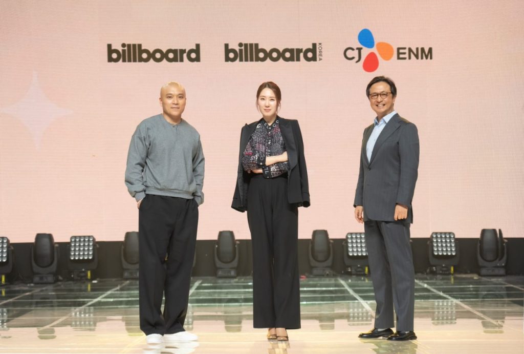 Three people in facing forward with the logo of billboard and cj enm at the back