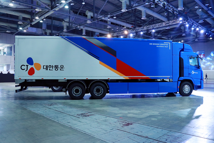 Blue and grey CJ Logistics automated parcel truck stands in large, well-lit warehouse.