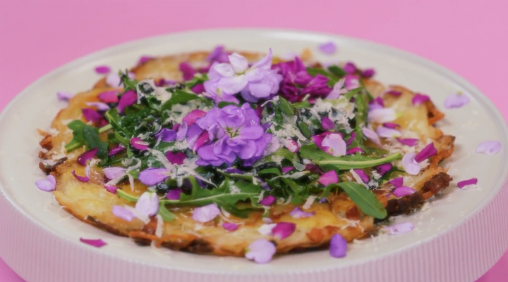 A hwajeon pizza topped with pink and purple flowers and greens sits on a white plate
