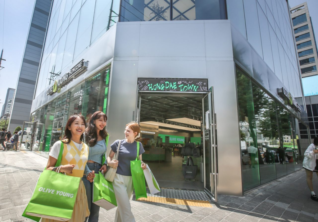  Three shoppers with shopping bags standing outside of the new Olive Young Hongdae Town location.


