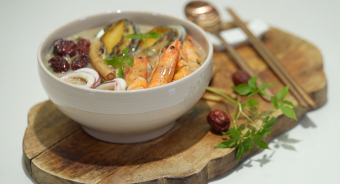 image of korean Chicken and seafood porridge  with shrimp and abalone on top of a wooden plate
