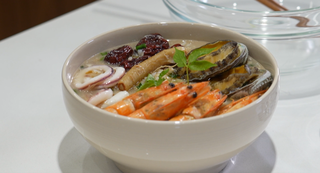 image of traditional korean Samgyetang (chicken and seafood soup) with shrimp, squid, and abalone on the surface of the bowl