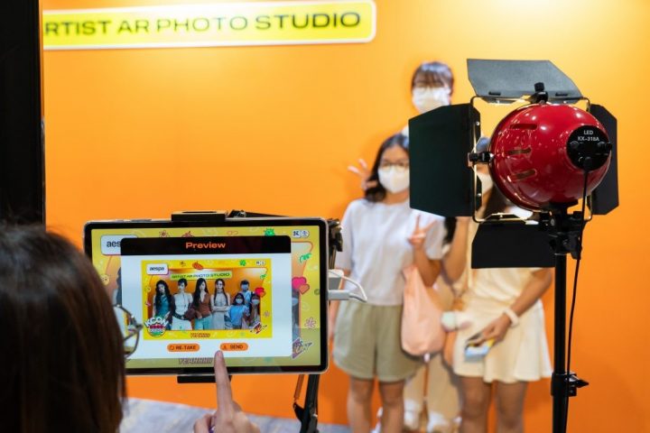 Photo of a booth with participants taking AR photos with their favorite artists, orange background.
