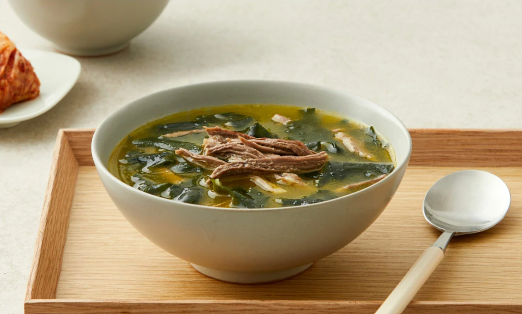image of seaweed soup on top of a wooden plate with a silver spoon on the right side