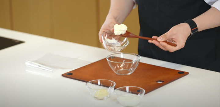 Cream cheese in a tablespoon that is being placed in a cup. 
