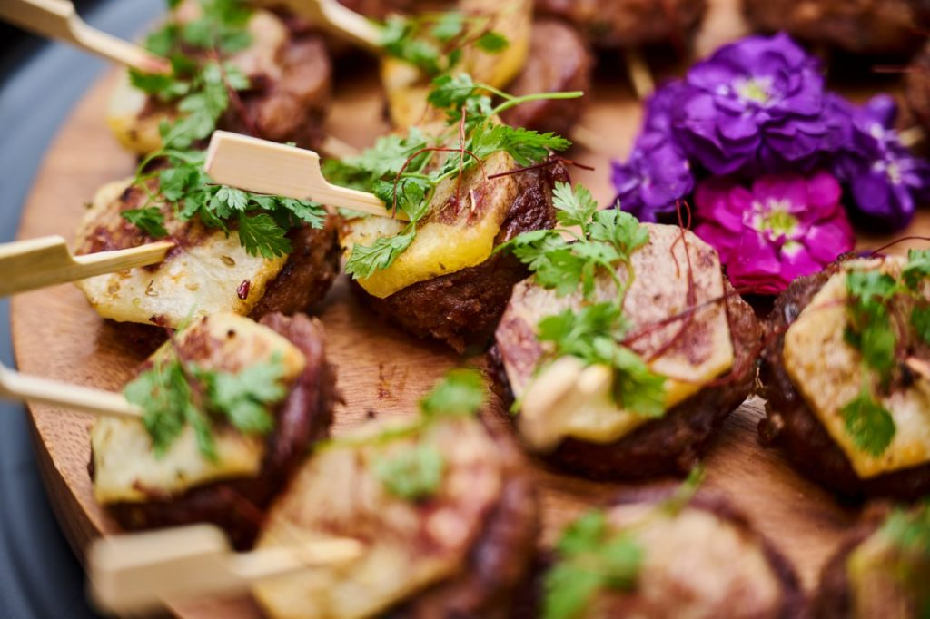 Tteokgalbi Skewers on top of wooden plate garnished with purple flower