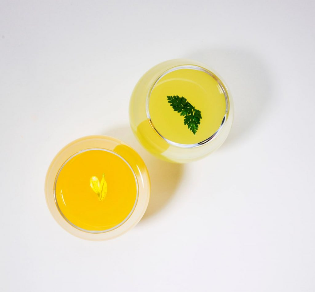 Orange-citrus colored Solabon cocktail next to the ldH cocktail, garnished with a green Korean mint leaf.