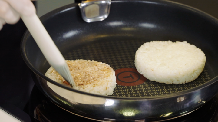 A chef brushes soy sauce glaze onto a rice bun. 
