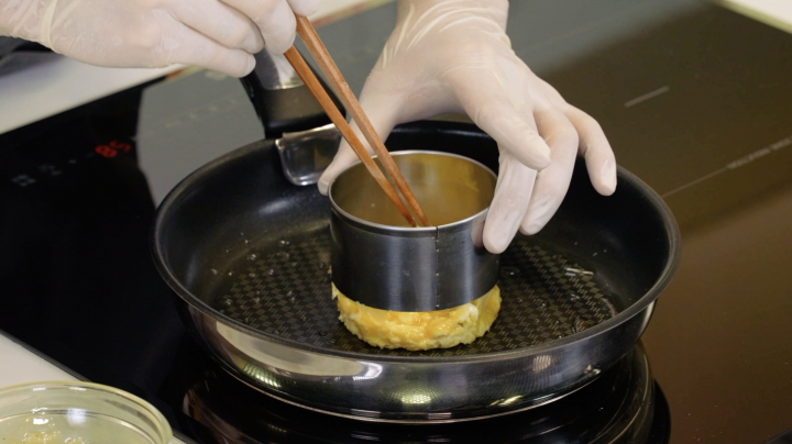 A chef cooks an egg patty using a round mold and a frying pan. 