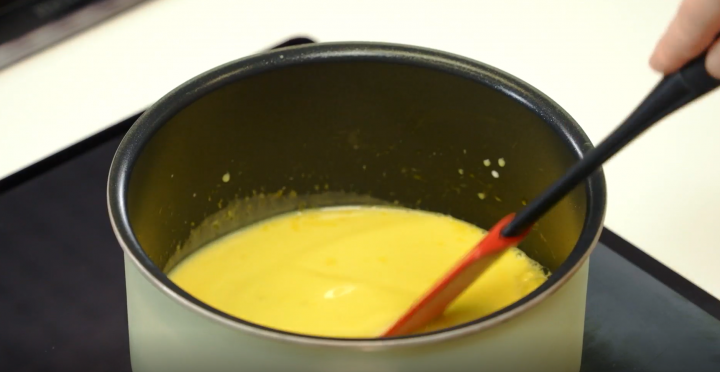 Egg yolk, milk and vanilla extract cooking inside a black pan and electric stove. 
