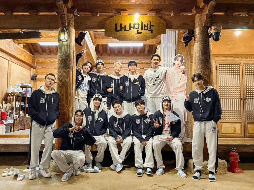 The members of SEVENTEEN posing in front of a minbak while all wearing the same tracksuit.