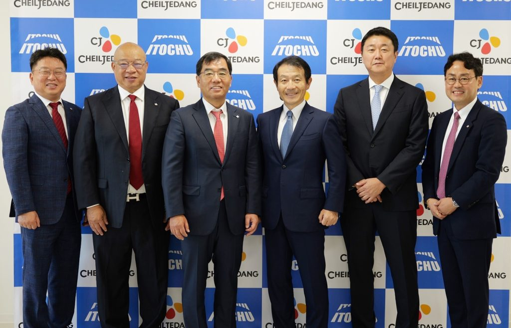 Six executives in business suits standing together and posing for a commemorative photo in front of a CJ CheilJedang and ITOCHU logo wall.
