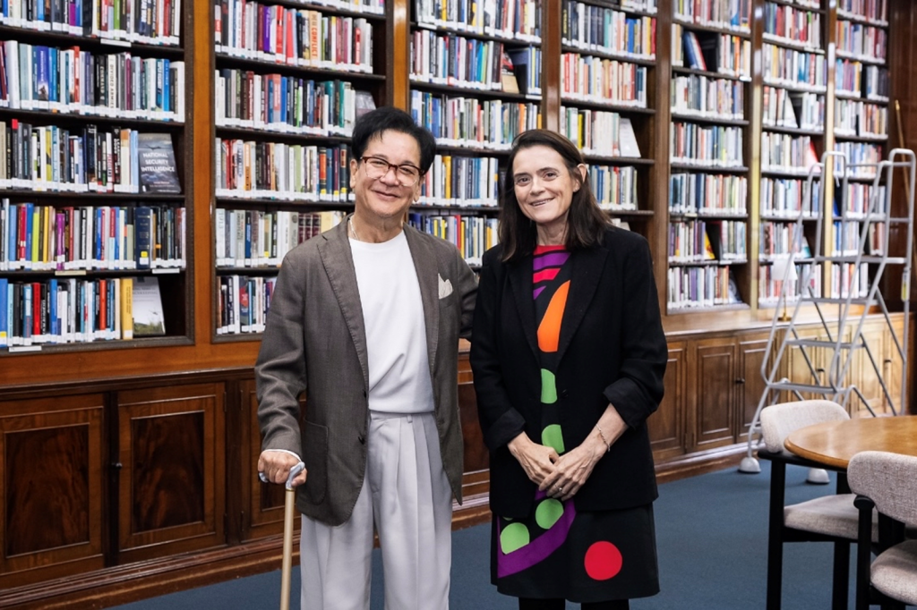 CJ Group Chairman Lee Jay-hyun and the Director of Chatham House Bronwen Maddox smile at the camera in front of shelves of books.
