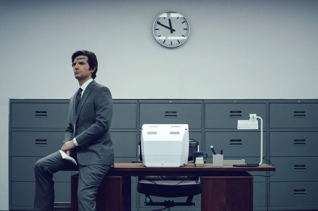 A poster for “Severance,” showing Adam Scott wearing a suit sitting on a desk in a muted office.