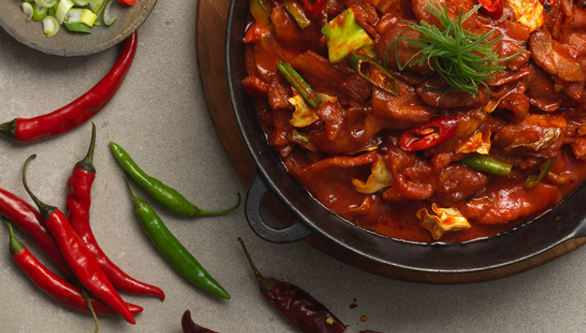 Spicy Korean dish next to red and green peppers 