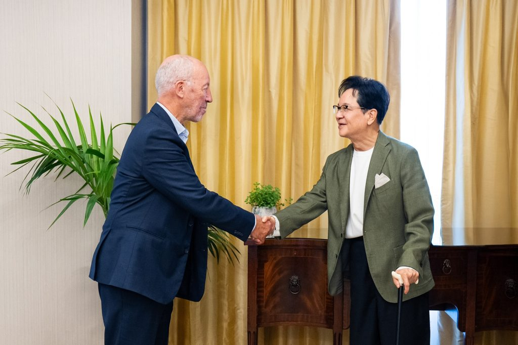CJ Group Chairman Lee Jay-Hyun shakes hands with sports marketing expert Michael Robert Payne in an office with yellow curtains
