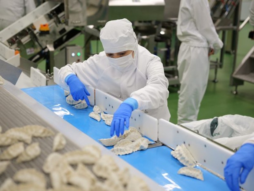 A masked worker in a white uniform sorts through bibigo Mandu in the Chiba facility.
