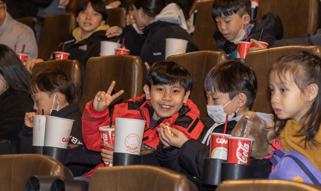 Several children sit in a theater with fountain drinks for the CJ Donorscamp “Sharing Seats” program.
