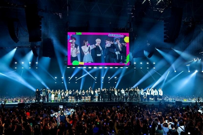 A large concert hall during a KCON event with several K-pop groups on stage in front of a crowded audience.
