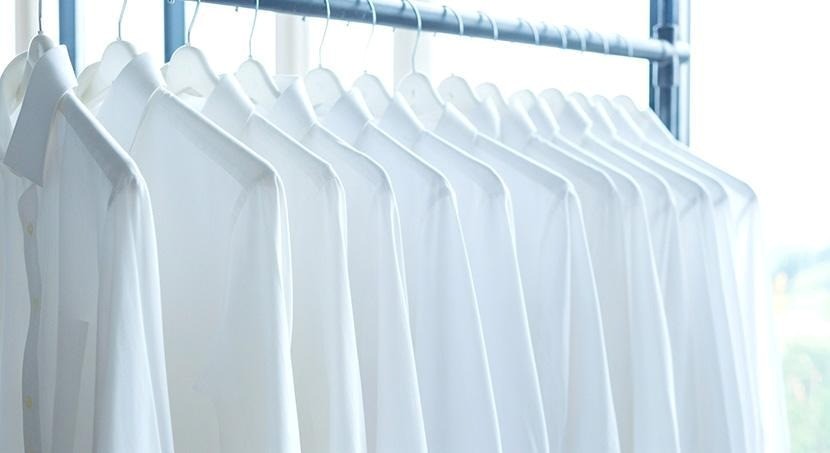 Several white button-up dress shirts hanging on coat hangers on a rack.
