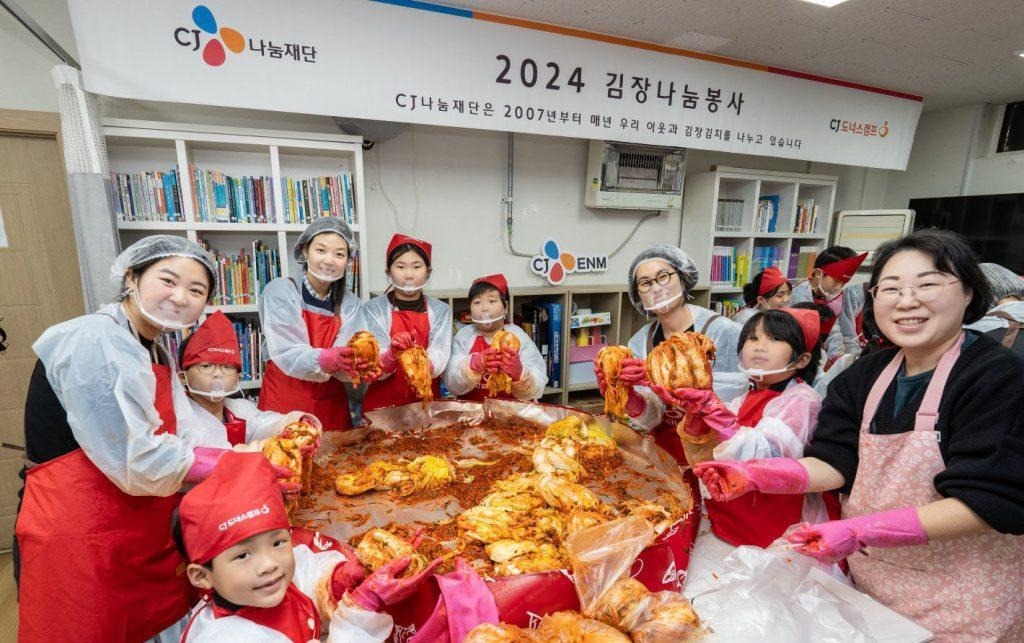 Several women and girls gather around a tub for a CJ Donorscamp kimchi-making volunteer event.
