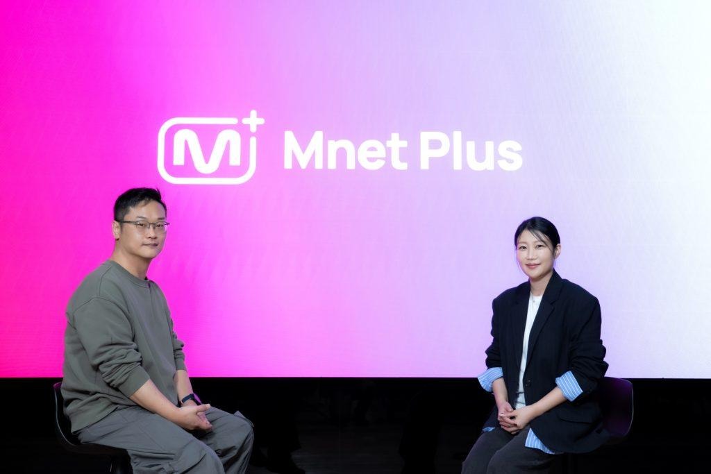 Cha Woojin and Kim Jiwon sit in front of a large pink Mnet Plus sign.