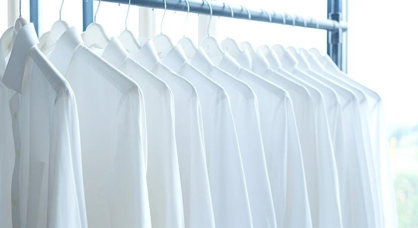 Several white button-up dress shirts hanging on coat hangers on a rack.