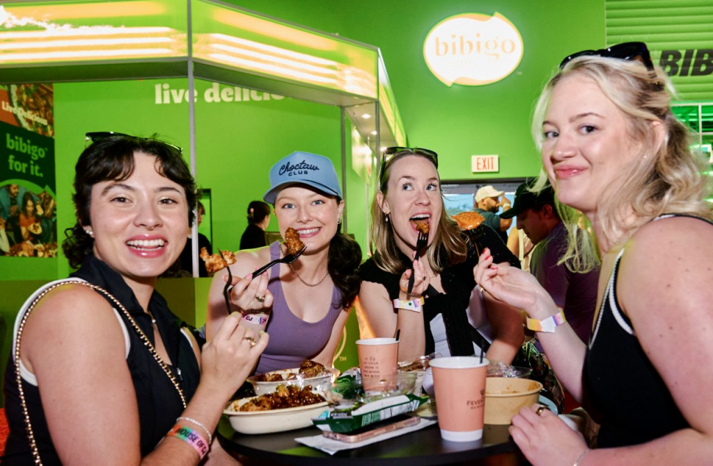 A group of four people eat bibigo food and smile at the camera
