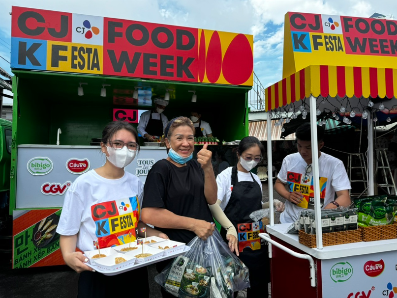 Customers stand in front of CJ food stands outside while holding samples and food
