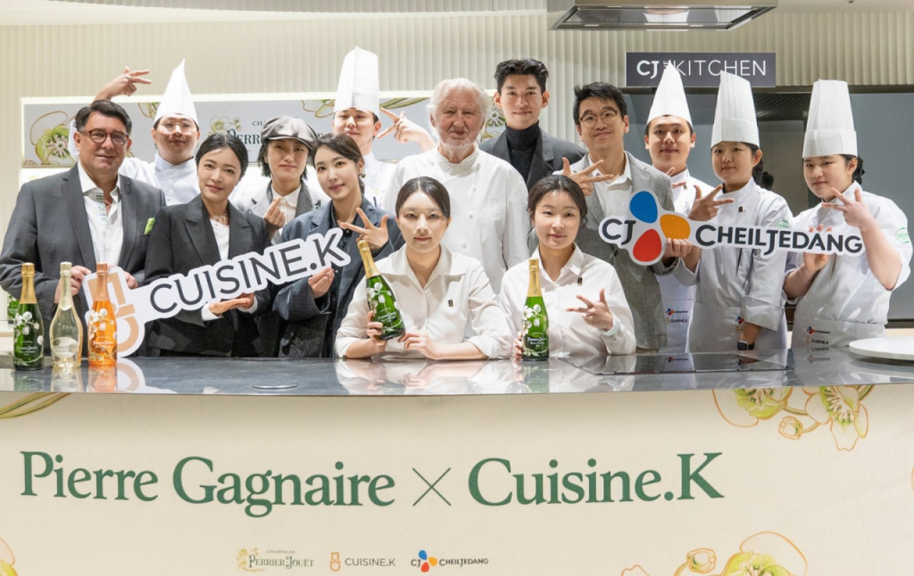 A group of chefs, including Pierre Gagnaire, celebrate with champagne at a table. The table reads: “Pierre Gagnaire x Cuisine.K.”

