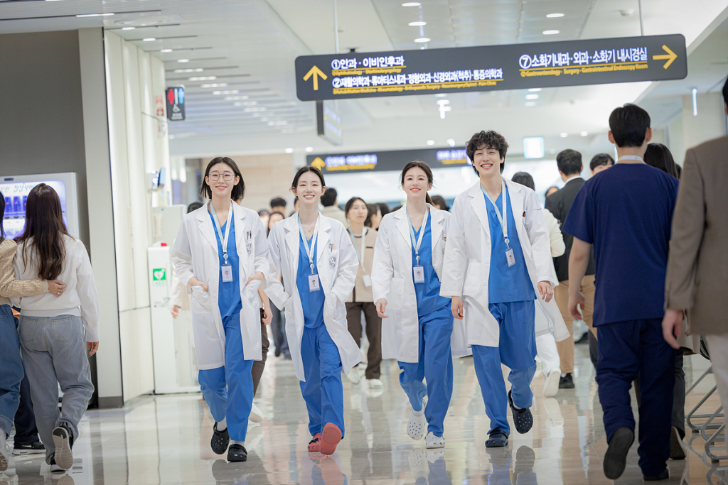 Cast members of Resident Playbook in medical attire, walking through a hospital hallway.