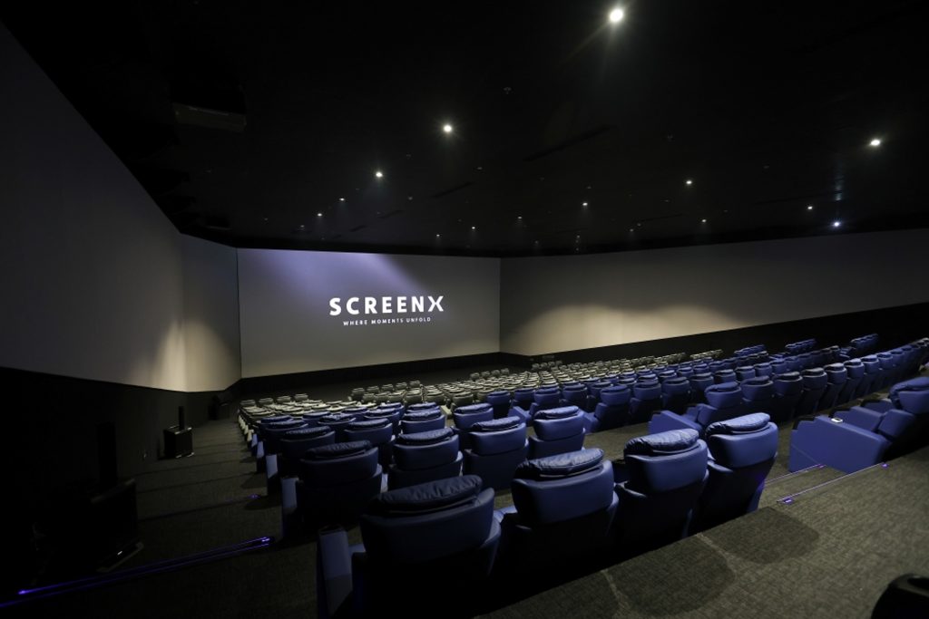 A wide view of a dimmed SCREENX theater from the back with empty seats.
