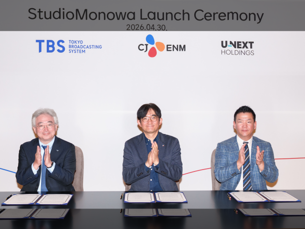 Three executives sit at a signing table during the StudioMonowa launch ceremony, with TBS, CJ ENM and U-NEXT Holdings logos displayed on the backdrop.