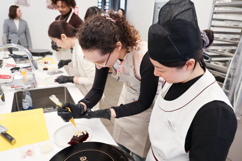 Participants in aprons garnish and plate a dish during a hands-on Cuisine.K class.