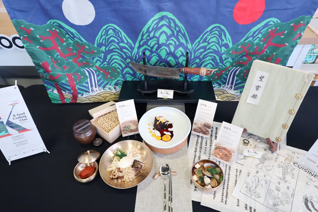 Display table with plated dishes, ingredients and printed materials from a Cuisine.K class.