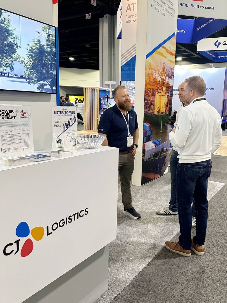 Three men stand talking by the CJ Logistics booth.