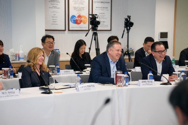 Several executives sit on one side of two rows of tables in a conference room during a meeting.