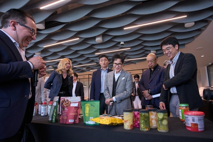 Chairman Lee Jay-hyun and other CJ and Schwan’s executives look at a spread of food on a table.