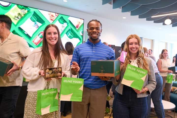 Three CJ and Schwan’s employees smile while holding gift bags and boxes from OLIVE YOUNG and TOUS les JOURS.