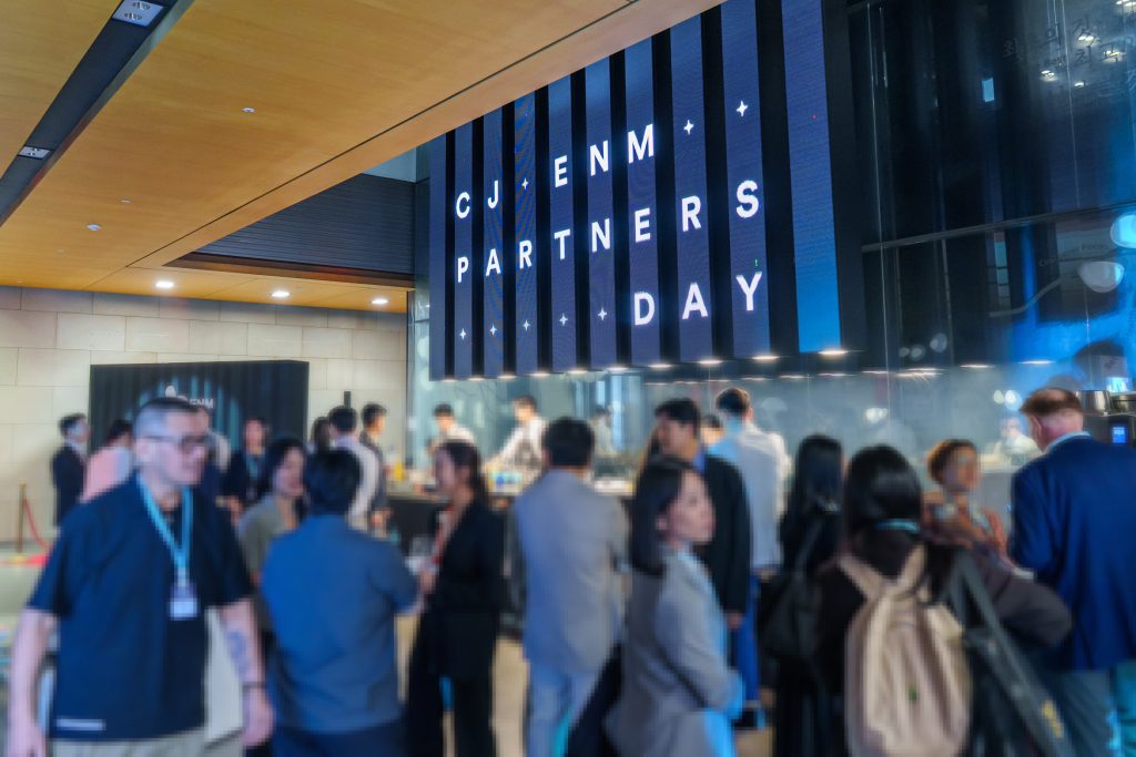 Guests network beneath a large digital CJ ENM Partners Day sign at the event venue.