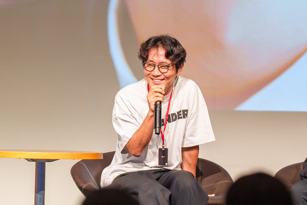 Director Park Shin-woo smiles while speaking into a microphone during the creator talk session.