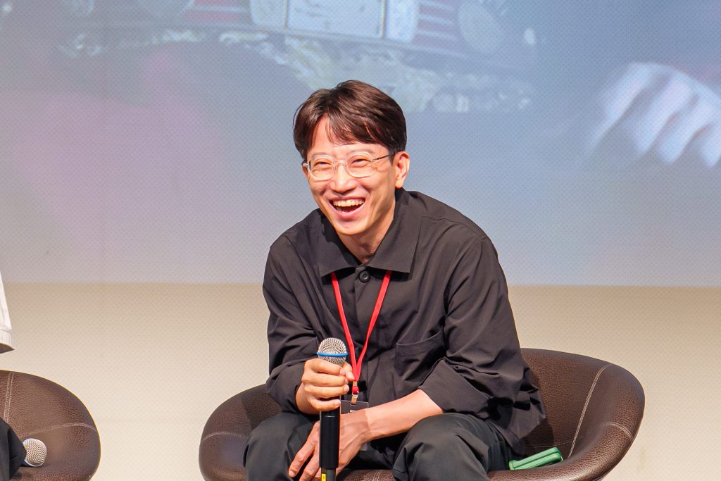 Director Jang Tae-yoo smiles while holding a microphone during the creator talk session.