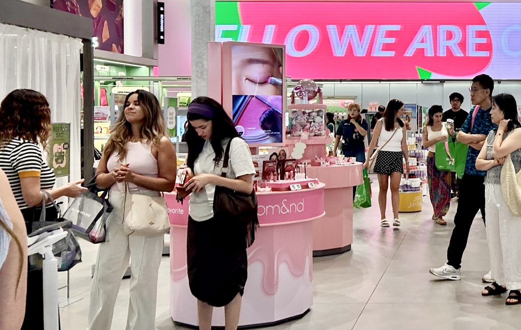 Shoppers at OLIVE YOUNG Pasadena walk around various skincare and makeup booths.
