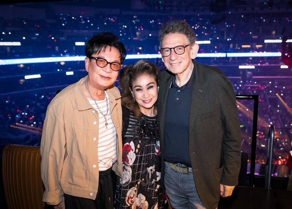 Three executives pose together at KCON LA 2026 with the concert stage in the background.