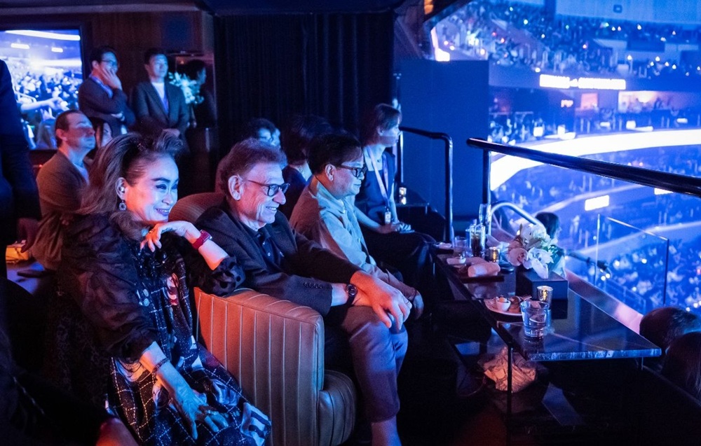 Three executives watch a KCON LA 2026 performance from a VIP viewing area.