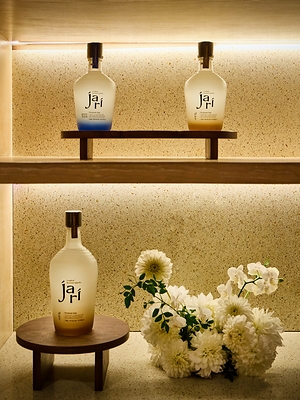 Three bottles of CJ Foods’ premium Korean spirits brand jari displayed on illuminated shelves with floral arrangements.